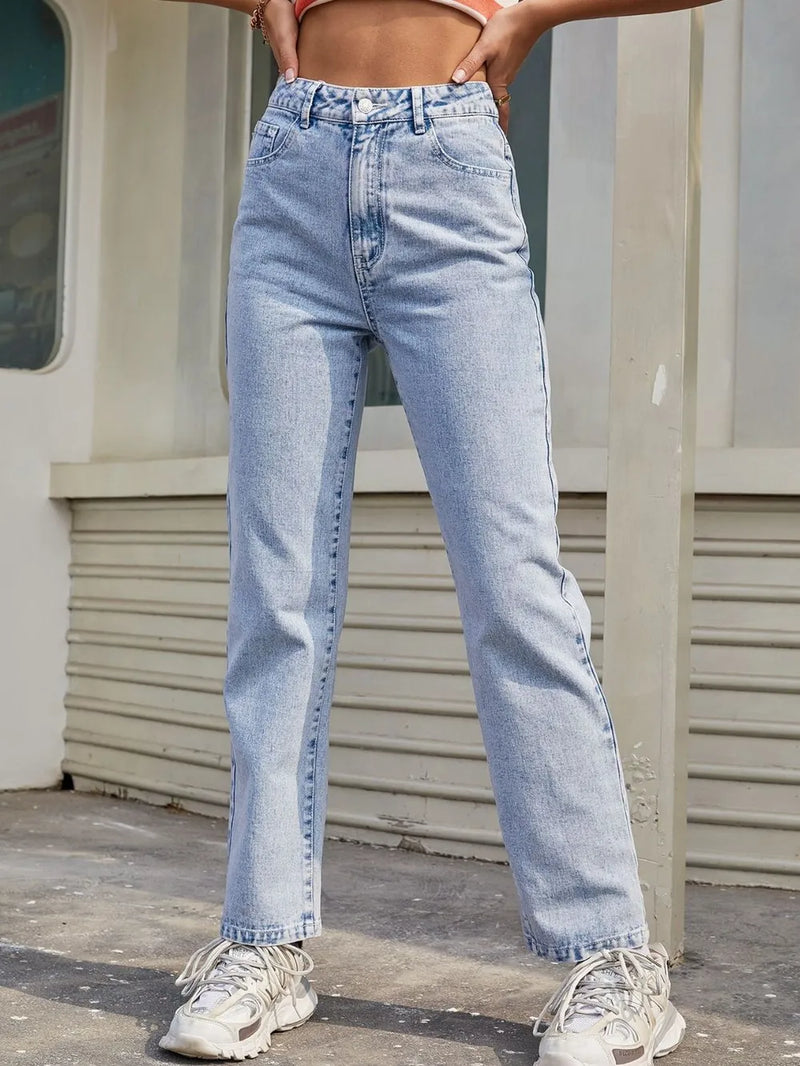 Person wearing light blue jeans and white sneakers standing against a neutral background