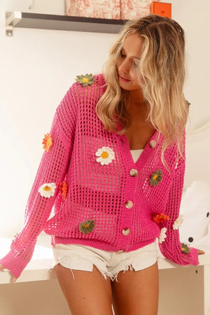 Woman wearing a pink crochet cardigan with floral embellishments indoors.