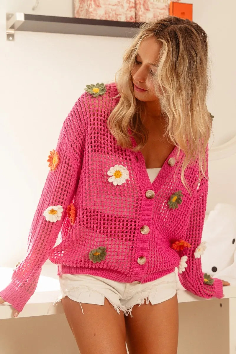 Woman wearing a pink crochet cardigan with floral embellishments indoors.
