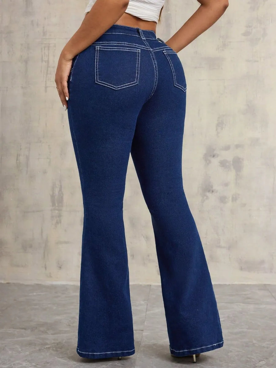 Blue flared jeans worn by a person against a gray concrete wall.