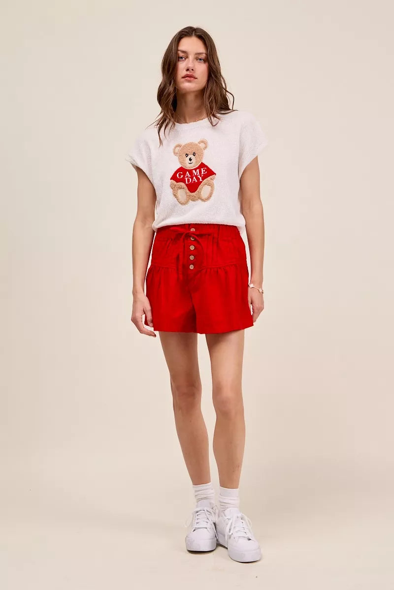 Woman wearing a white t-shirt with a teddy bear graphic and red shorts on a beige background