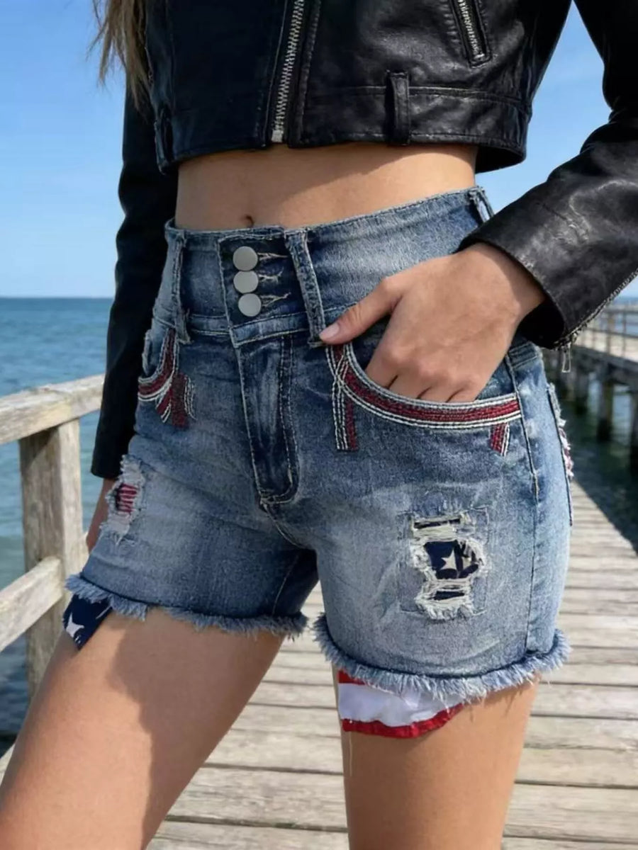 Person wearing distressed denim shorts and a black leather jacket on a wooden pier by the ocean.