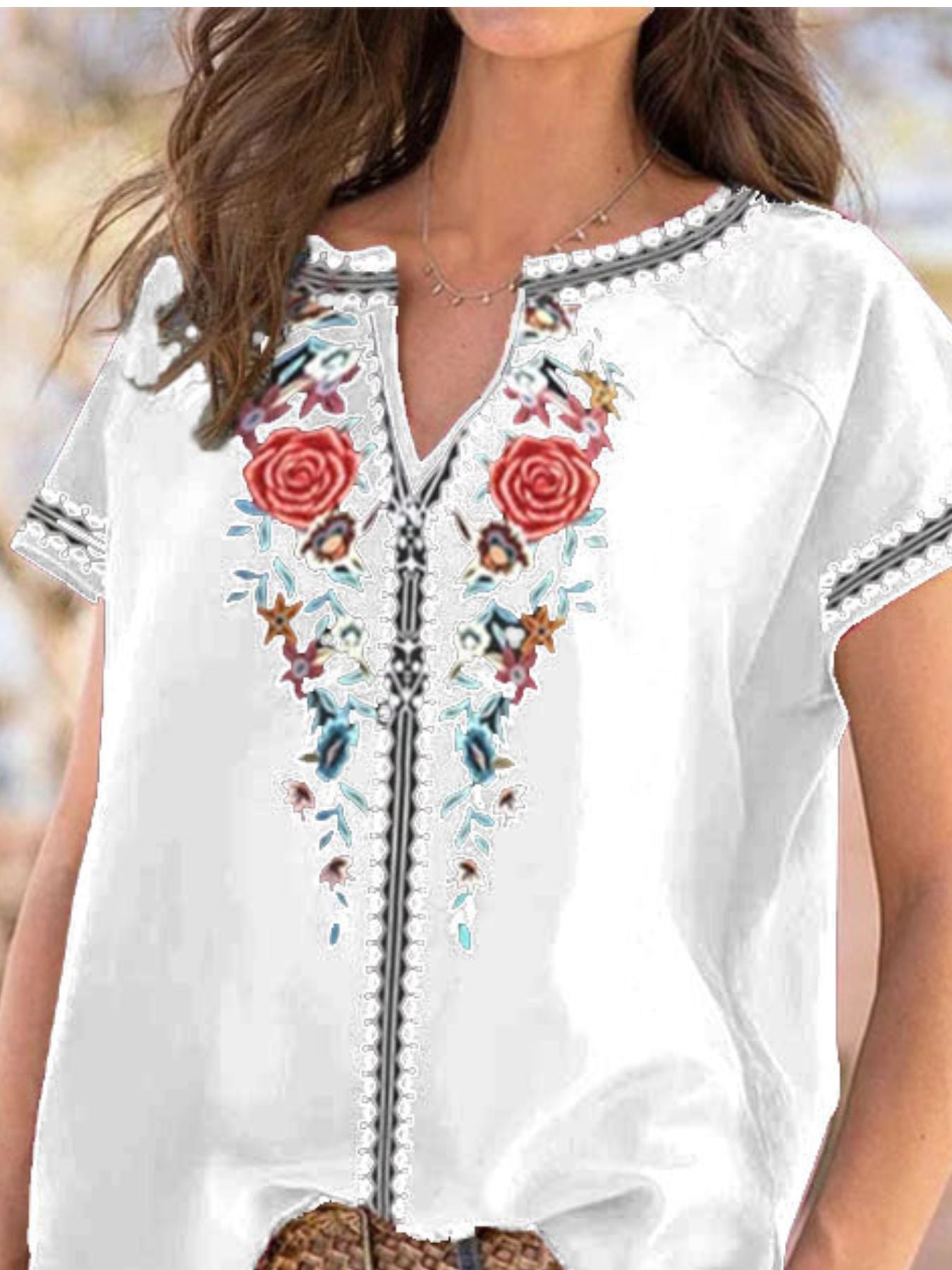 White blouse with colorful floral embroidery on a blurred natural background