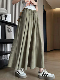 Person wearing a long green skirt and white sneakers in an indoor setting