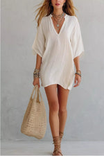 Woman wearing a white dress holding a straw bag against a plain background