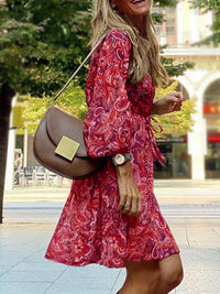Woman in a red patterned dress holding a brown handbag on a city street.