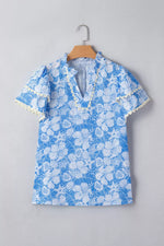 Blue floral blouse with white accents on a wooden hanger against a gray background