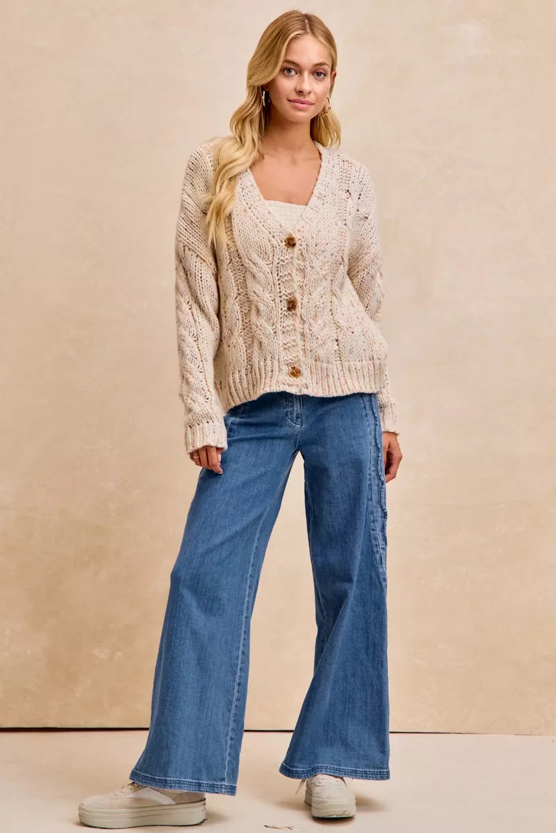 Woman wearing a beige cardigan and blue jeans against a beige background
