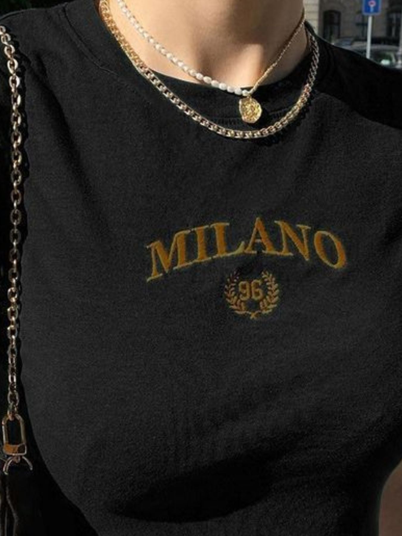 Black sweatshirt with 'MILANO 96' embroidery and gold necklace.