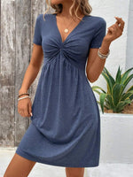 Woman wearing a blue dress with a wooden wall and plant in the background