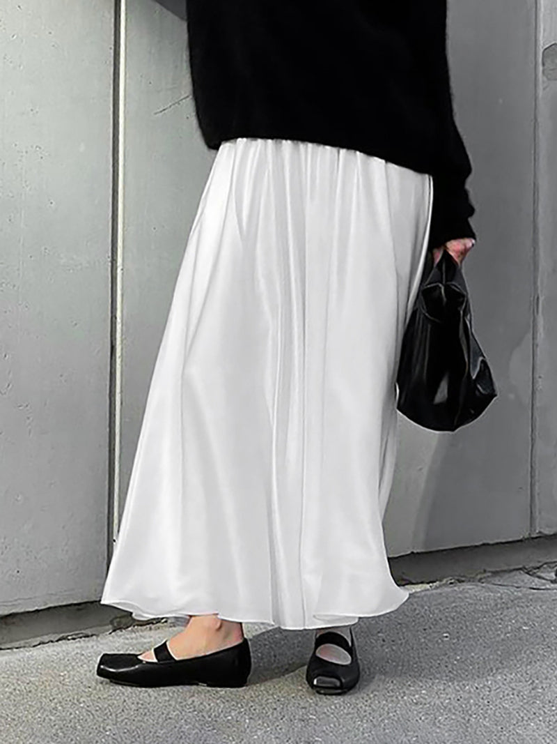 Person wearing a black top, white skirt, and black shoes against a gray wall.