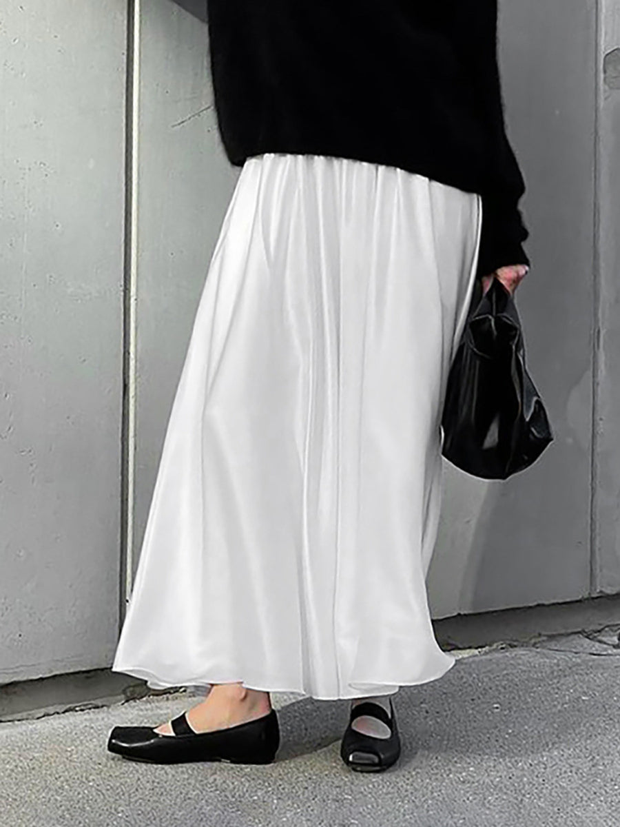 Person wearing a black top, white skirt, and black shoes against a gray wall.