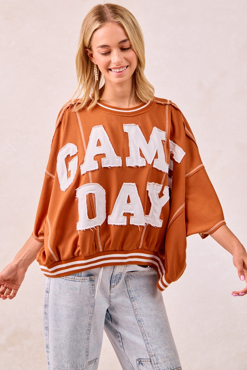 Woman wearing a 'GAMEDAY' oversized sweater with a plain background