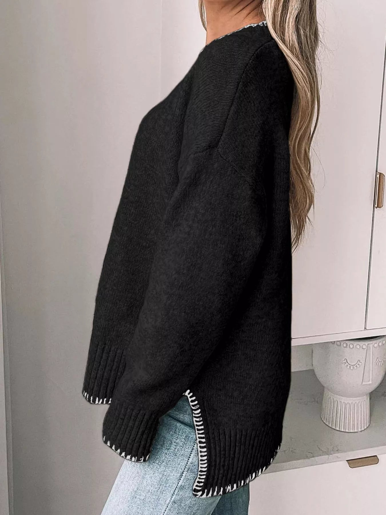 Person wearing a black sweater with white trim, standing against a neutral background.