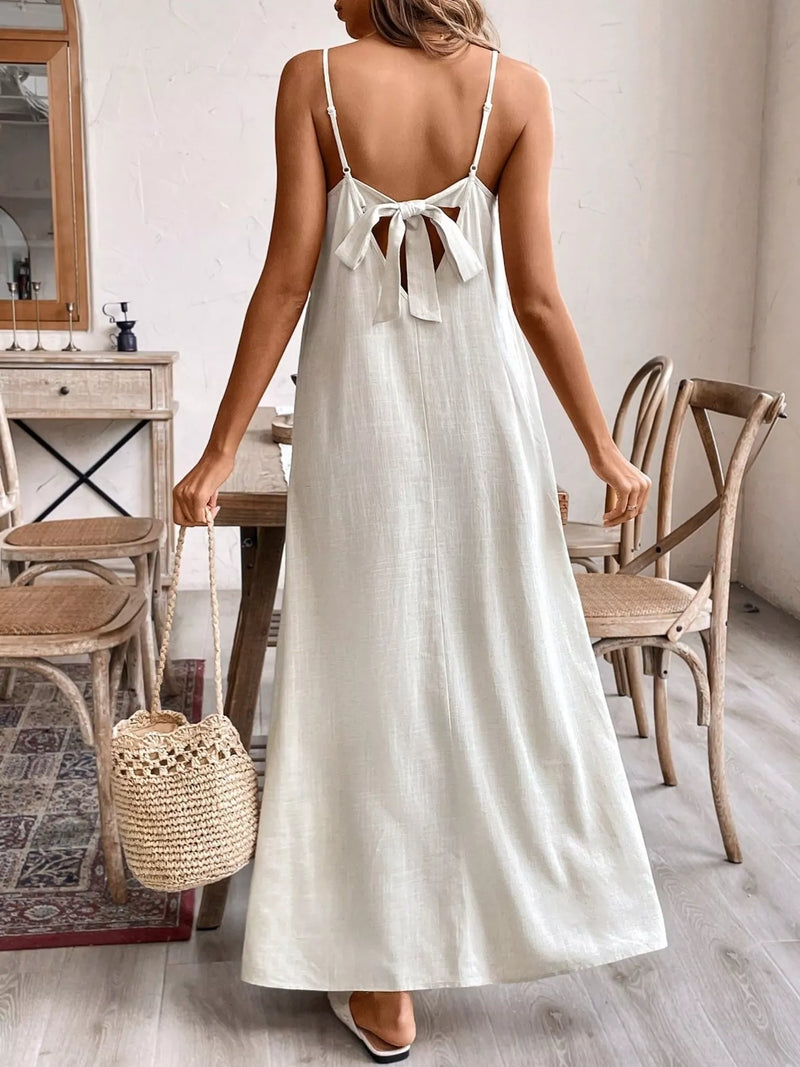 Woman in a white dress holding a straw bag in a room with wooden furniture.