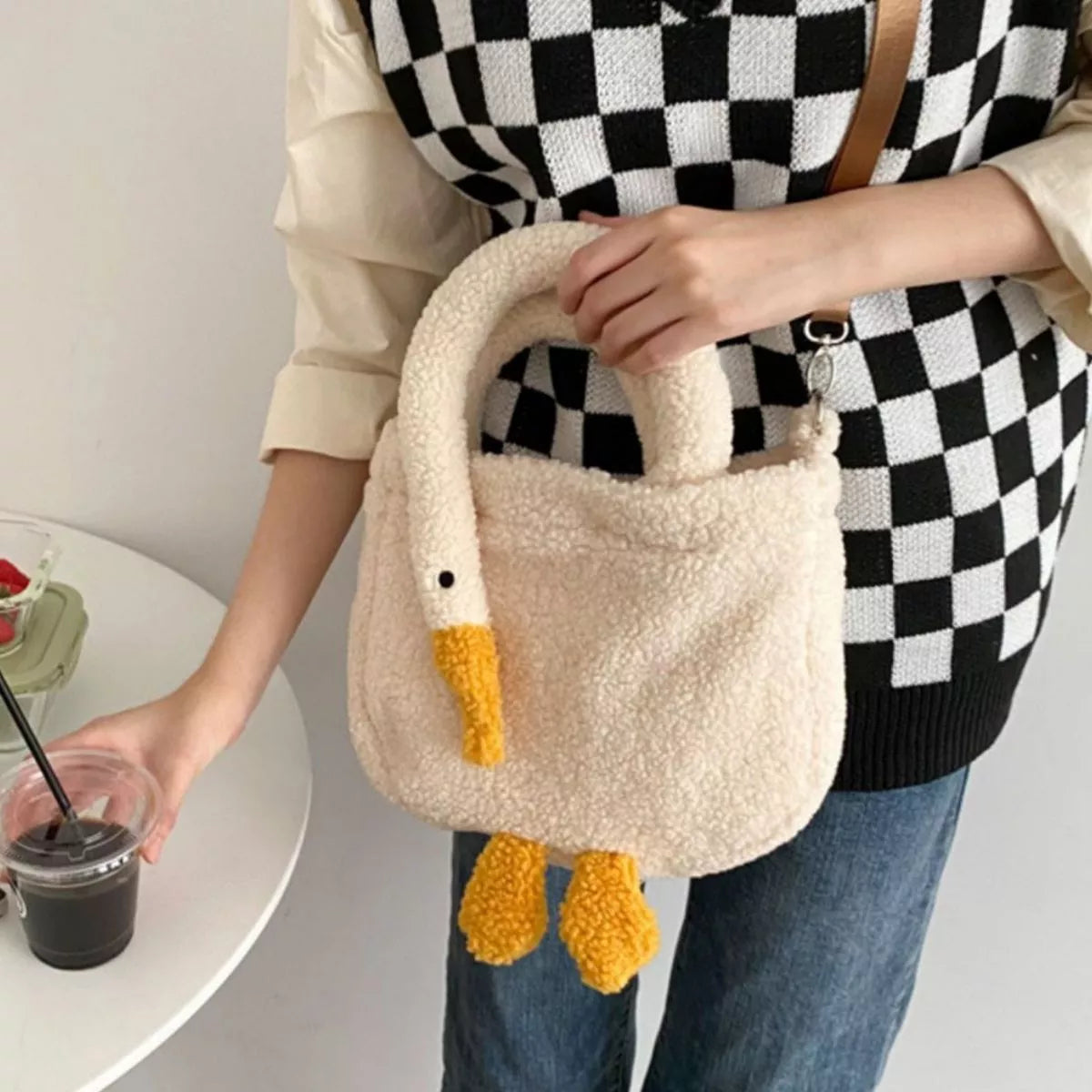 Person holding a fluffy goose-shaped handbag with a checkered sweater and jeans.