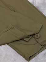 Close-up of olive green trousers folded on a textured light gray surface, showing a buttoned flap pocket and fabric texture.