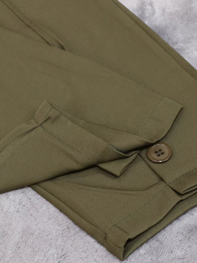 Close-up of olive green trousers folded on a textured light gray surface, showing a buttoned flap pocket and fabric texture.