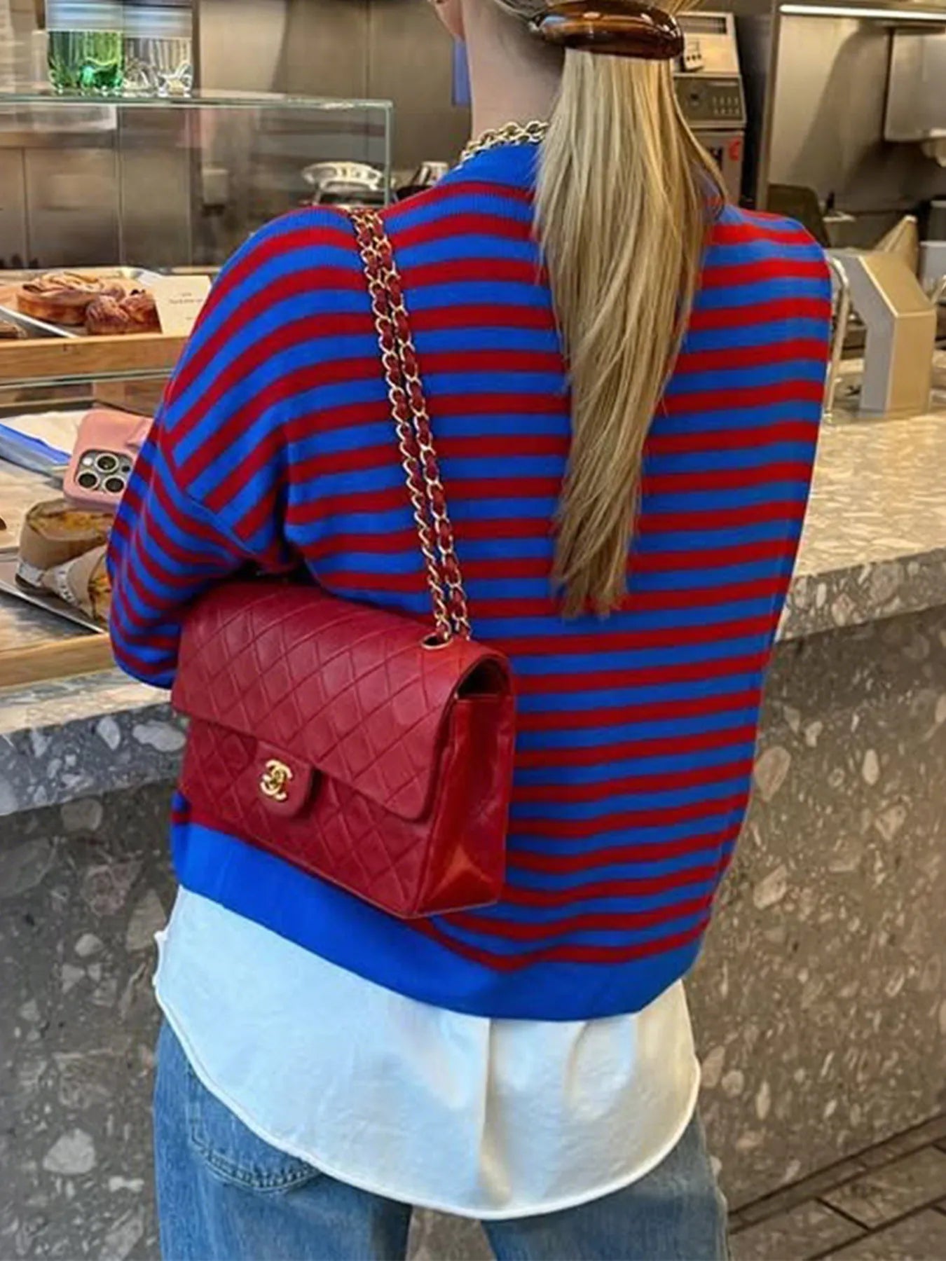 Person wearing a red and blue striped sweater with a red handbag in an indoor setting.