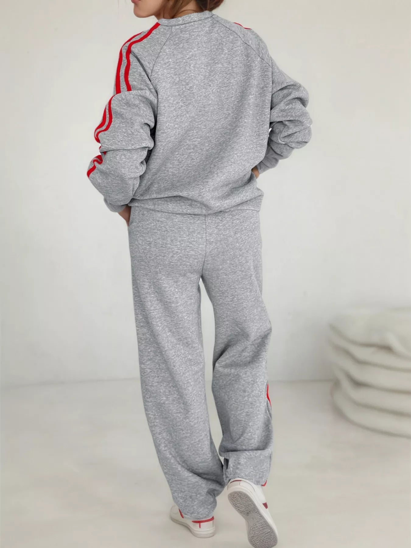 Person wearing a gray tracksuit with red stripes on a white background