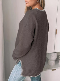 Person wearing a gray sweater with fringe details in a minimal indoor setting.