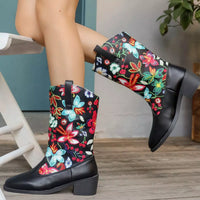 Black rain boots with colorful floral and butterfly patterns worn by a person.