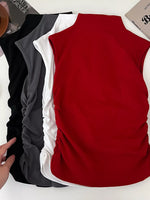 Red sleeveless top with black and white shirts underneath on a white surface.
