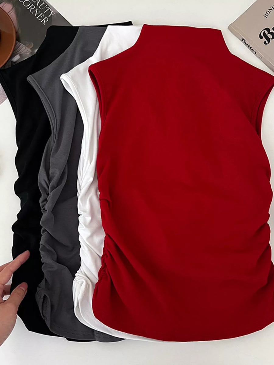 Red sleeveless top with black and white shirts underneath on a white surface.