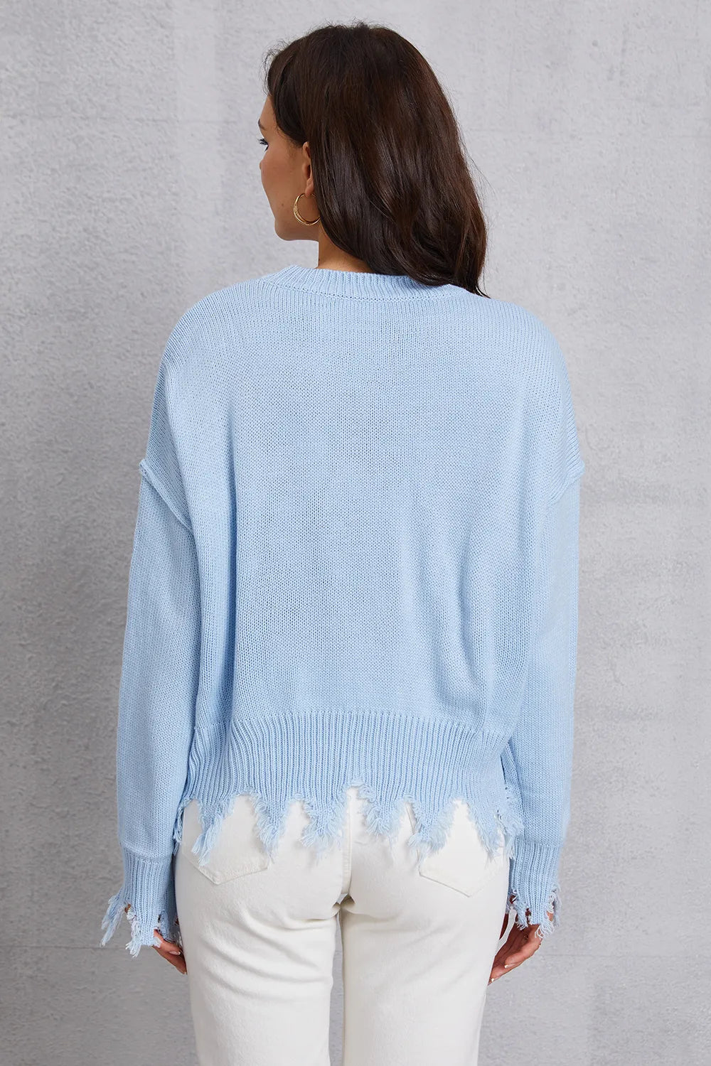 Light blue distressed sweater worn by a person against a gray background