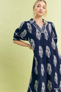 Woman wearing a navy dress with white patterns against a light green background