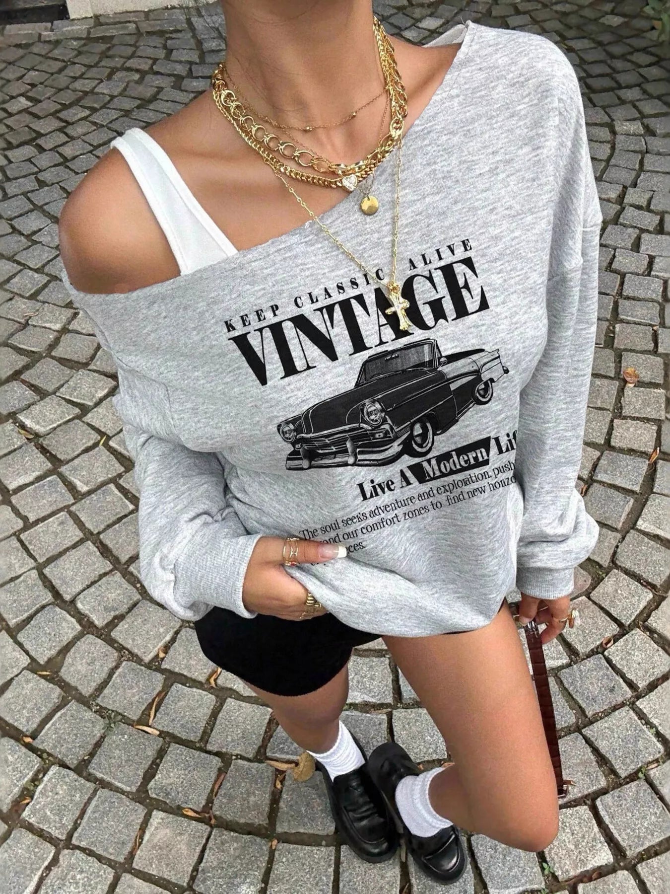 Person wearing a gray sweatshirt with vintage car graphic on a cobblestone street.