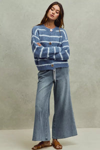 Woman wearing a blue striped sweater and denim jeans against a neutral background