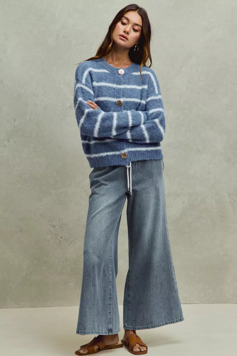 Woman wearing a blue striped sweater and denim jeans against a neutral background