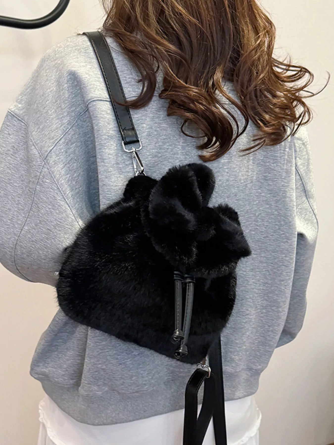 Person wearing a gray sweater with a black fluffy backpack