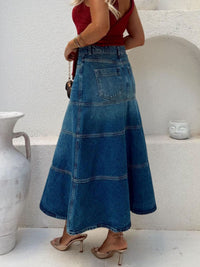 Person wearing a long blue denim skirt with a white background