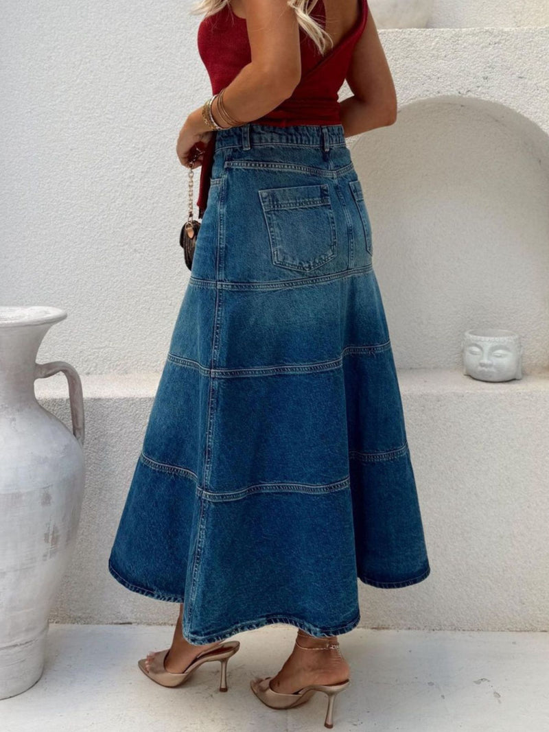 Person wearing a long blue denim skirt with a white background