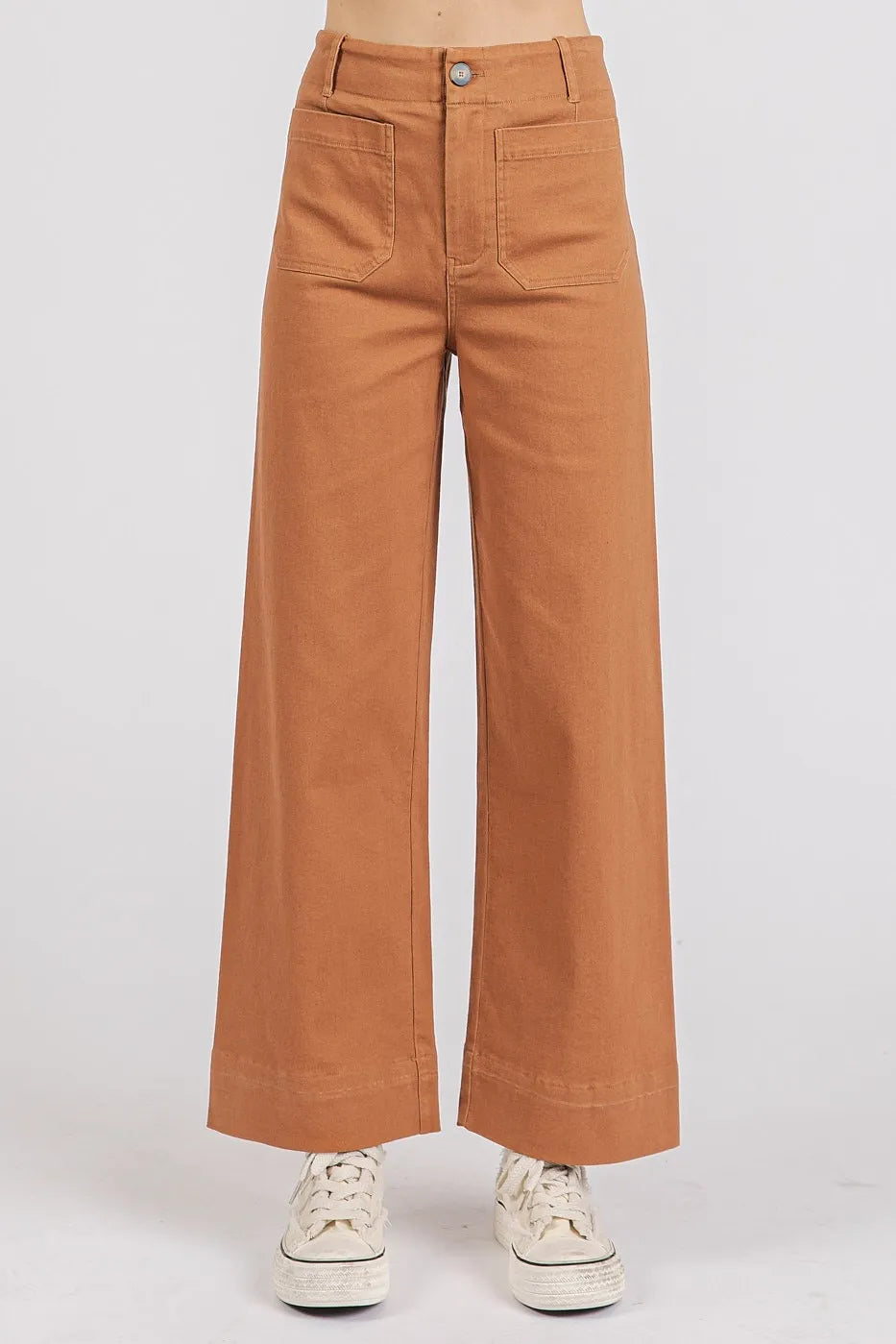 Brown wide-leg pants worn with white sneakers on a light gray background