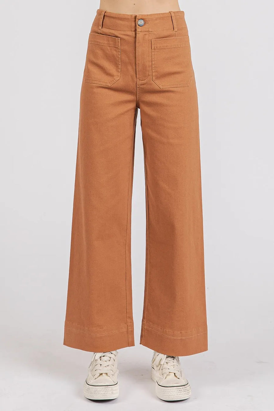 Brown wide-leg pants worn with white sneakers on a light gray background