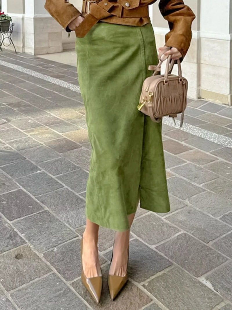 Person wearing a green skirt and brown jacket with a matching handbag on a stone pavement.