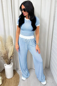 Woman wearing a light blue outfit with white drawstring pants, standing indoors.