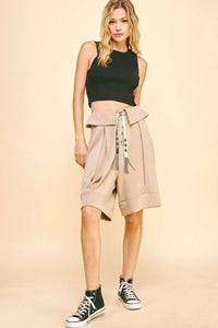 Woman wearing a black crop top and beige paperbag waist shorts on a beige background