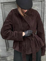 Person wearing a brown coat and black gloves against a gray stone wall.