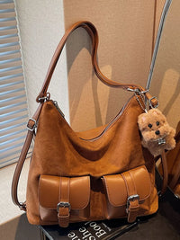 Brown leather handbag with a teddy bear charm on a surface.