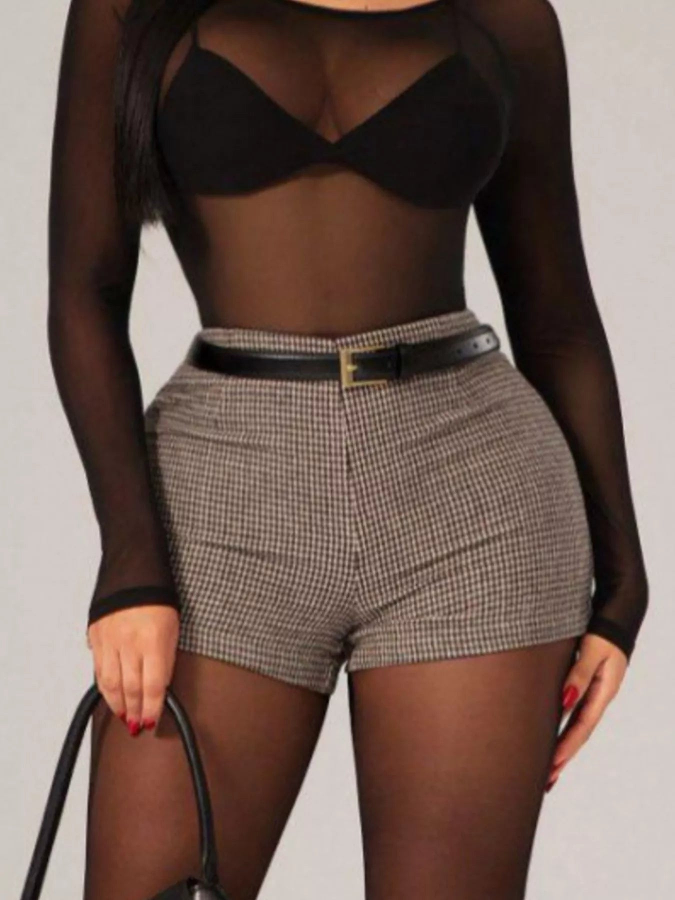 Person wearing a black sheer top and plaid shorts on a plain background