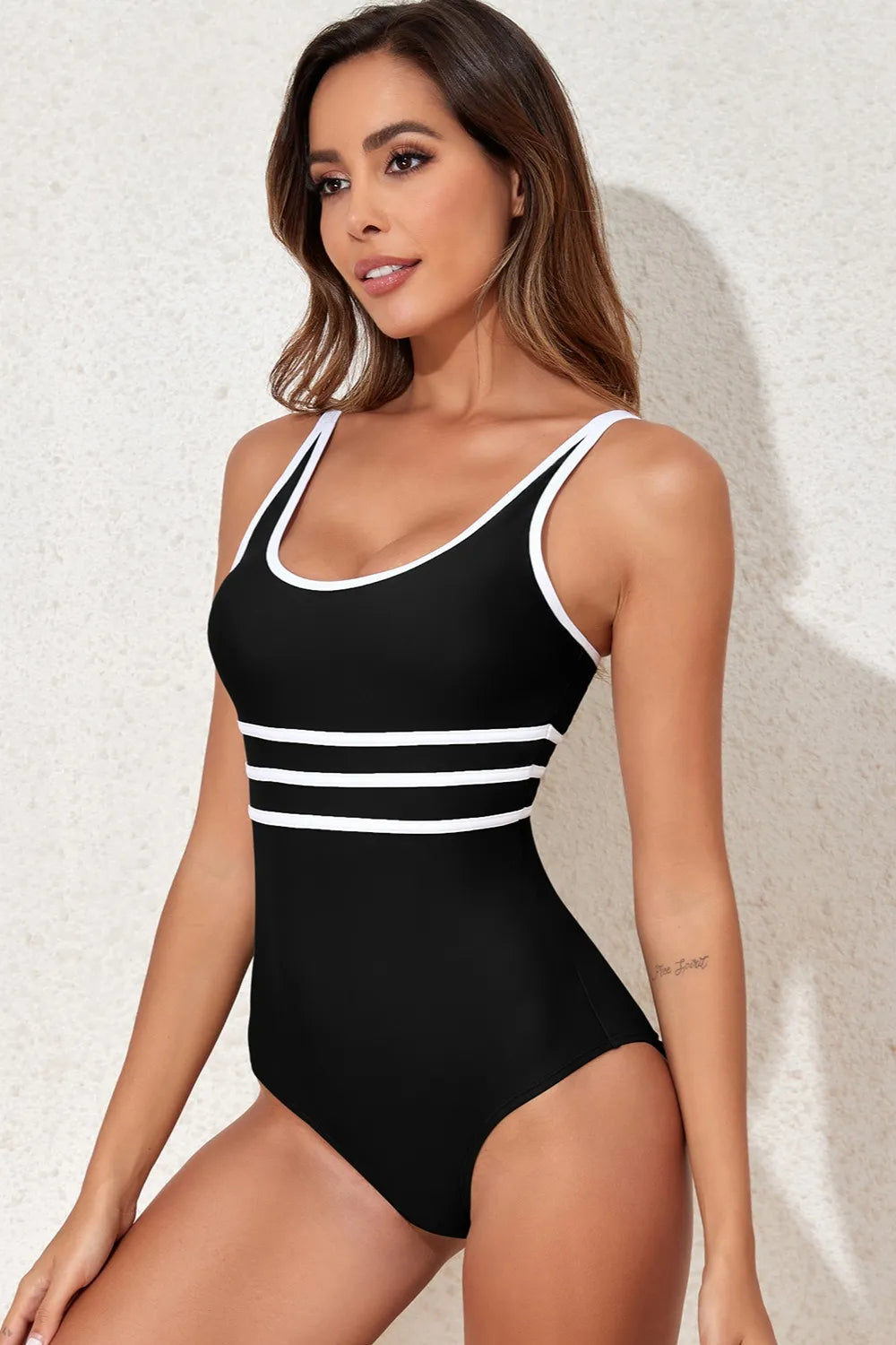 Woman wearing a black swimsuit with white stripes against a textured white background