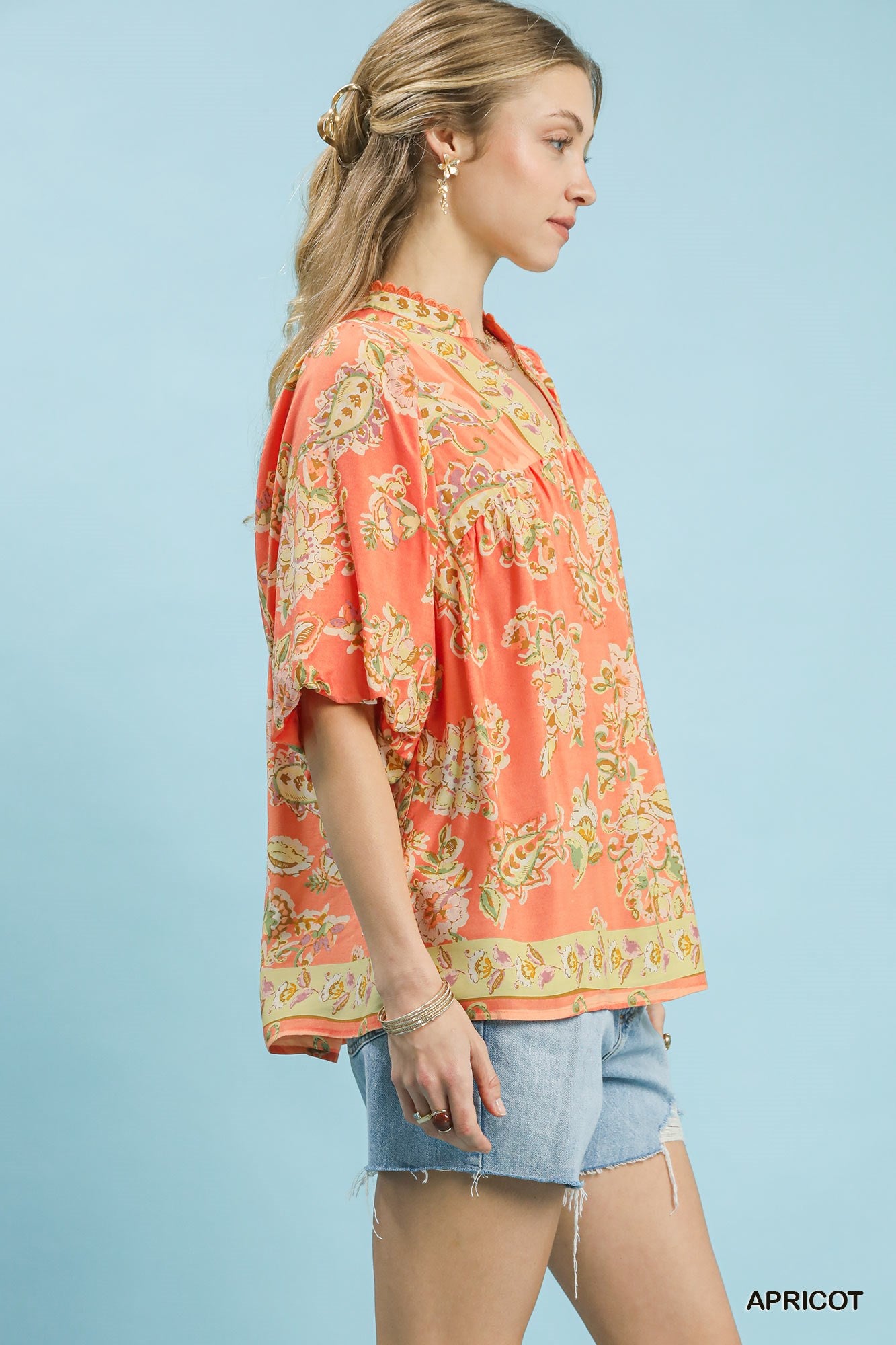 Woman wearing a patterned apricot shirt against a light blue background