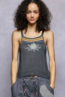 Woman wearing a dark gray tank top with floral embroidery on a gray background