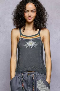 Woman wearing a dark gray tank top with floral embroidery on a gray background