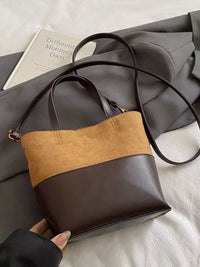 Two-tone brown and black handbag held by a person on a light gray surface with a book in the background.
