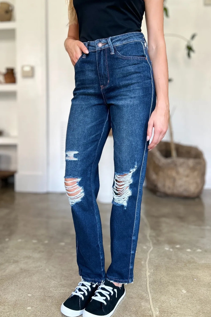Person wearing blue distressed jeans and black sneakers indoors.